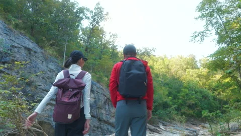 Two asian hiker stands on a light colored rock beside a gentle flowing stream Video stock 342410139