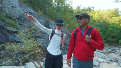 Two asian hiker stands on a light colored rock beside a gentle flowing stream Video stock 342410188