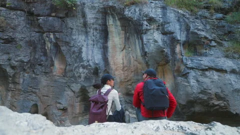 Two asian hiker stands on a light colored rock beside a gentle flowing stream Video stock 342410327