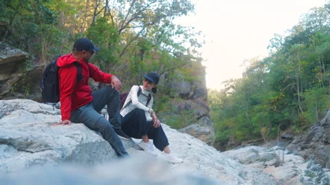 Two asian hiker stands on a light colored rock beside a gentle flowing stream Stock Footage 342410390