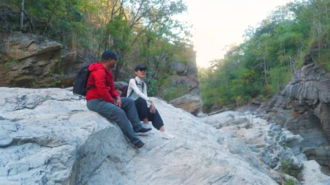 Two asian hiker stands on a light colored rock beside a gentle flowing stream Video stock 342410419