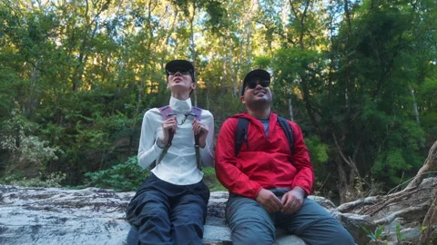 Two asian hiker stands on a light colored rock beside a gentle flowing stream Video stock 342410867