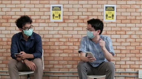 Two Asian men wearing face masks sit socially distancing. Stock Footage 157519503