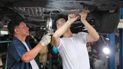 Two Asian men wearing helmets work at a mechanics garage. In the workshop, a tea Stock Footage 216538784