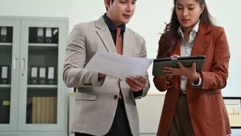 Two Asian professionals discussing documents in a modern office. Perfect fo.. Stock Footage 313461147