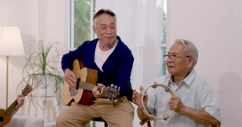 Two Asian senior men sing, smile and play guitar with tambourine during music Stock Footage 346356165