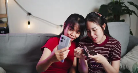 Two Asian siblings sit on a sofa and use cell phone to talk to friends  Video stock 305217426