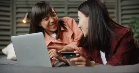 Two asian sisters lying on bed with laptop, having online shopping, cheerfully Stock Footage 108820051