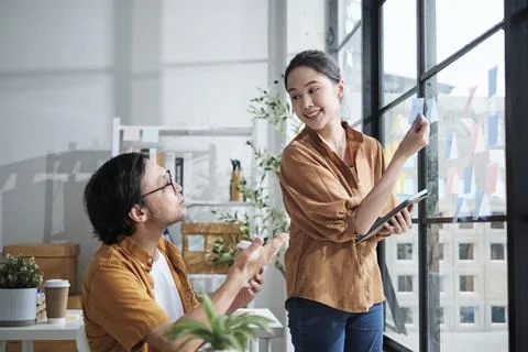 Two Asian startup partners are brainstorming at casual small business office. Фото