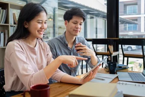Two Asian students learning together with a laptop and tutor together at cafe Stock Photos