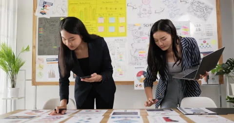 Two asian women checking to task on workplace desk while standing in office.  Stock Footage 201908481