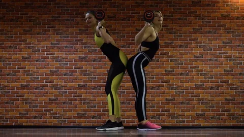 Two athletic girls squat with mini barbells and touch each other's buttocks. Stock Footage 116387733
