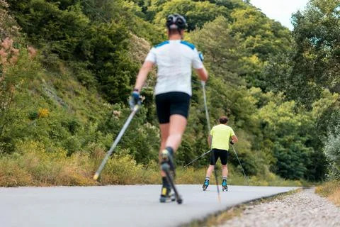 Two athletic men training on the roller ski at country road, back view. Defoc Stock Photos