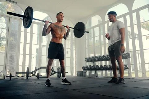 Two athletic multiracial young men in sports clothing doing weightlifting at the Stock Photos