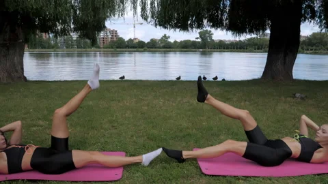 Two athletic young girl train the abdominal muscles, using their arms and legs Stock Footage 163923754