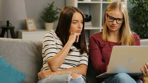 Two attaractive female friends having video chat on the laptop while sitting on Stock Footage 81925210
