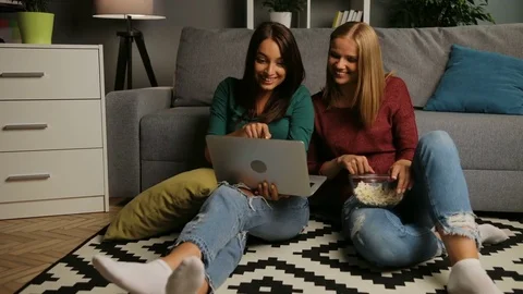 Two attaractive female friends with popcorn looking on the laptop while sitting Stock Footage 81934660