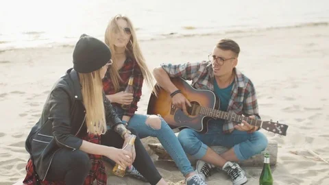 Two attractive blondes and a guy in glasses are sitting on a log, a guy is Video stock 75682099