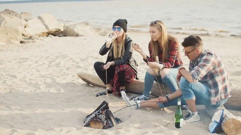 Two attractive blondes and a guy with glasses and a plaid shirt fry marshmallows Stock Footage 75685734