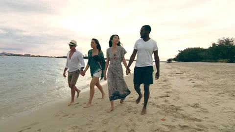 Two attractive couples, holding hands, walking on the beach under a cloudy sunse Stock Footage 199456306