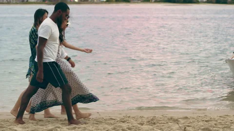 Two attractive couples, holding hands, walking on the beach at dusk with a boat Stock Footage 199458352