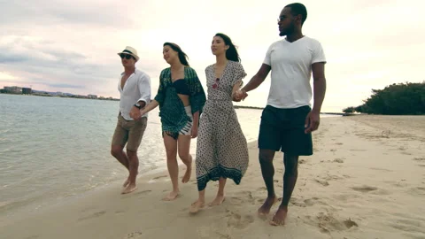 Two attractive couples, holding hands, walking on the beach, talking and smiling Stock Footage 199460664