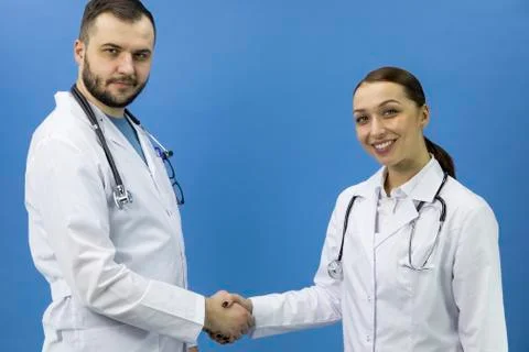 Two attractive doctors shaking hands on blue background, deal, collaboration Stock Photos