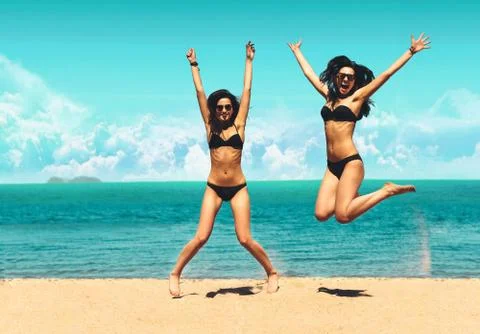 Two Attractive Girls in Bikinis Jumping on the Beach. Best Friends Having Fun Stock Photos