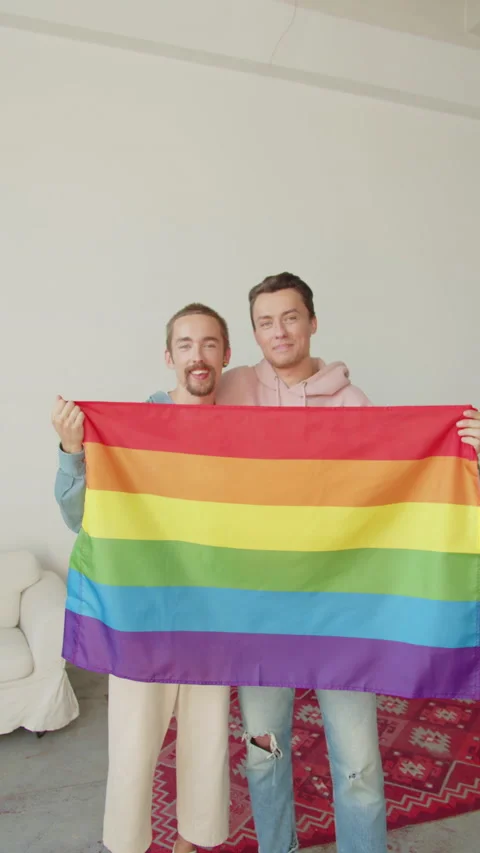 Two attractive men are showing lgbt flag, looking at each other and smiling Stock Footage 173903384