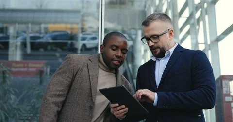 Two attractive mixed races men discussing business issues with a tablet computer Stock Footage 100447510