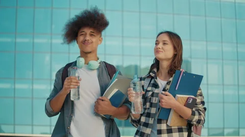 Two Attractive Students Drink Water from Bottle on Background of University. Stock Footage 241226953