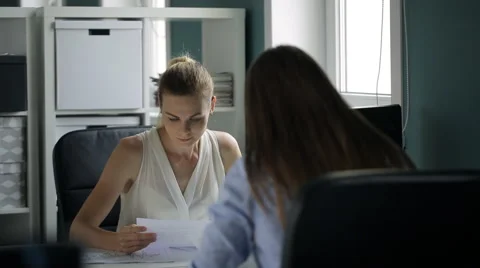 Two attractive women sit at table and look through documents in office Stock Footage 65310792
