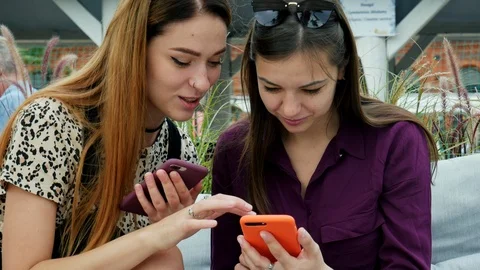 Two attractive young women using mobile phones and talking. Friends enjoying Stock Footage 116135692