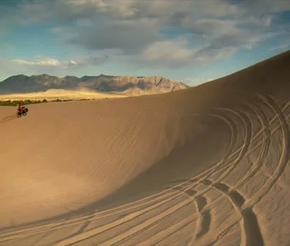Two ATV riders Circle large sand dune Stock Footage 21634895