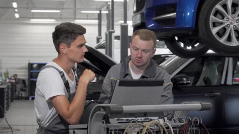 Two auto mechanics collaborating on car diagnostics with a laptop in the garage Stock Footage 311982803