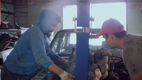 Two auto mechanics extract the motor from the hood of the car with the help of a Stock Footage 78826467