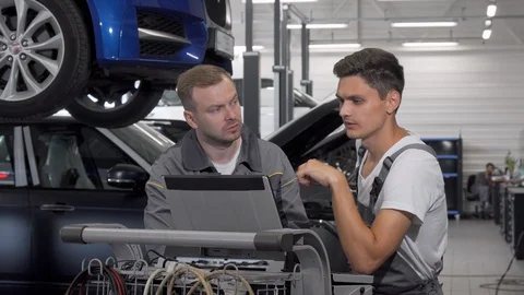 Two auto mechanics talking at the garage using laptop in car diagnostics Stock Footage 115579038