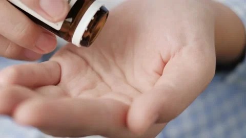 Two average size white round pills fall into palm of hand from pill bottle Stock Footage 147188708