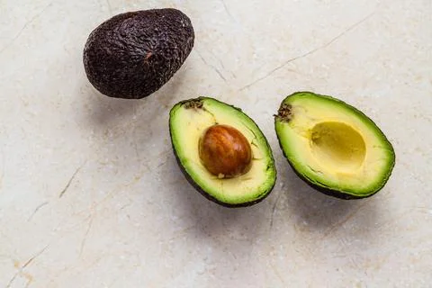 Two avocado pears, one cut open, marble background. Stock Photos