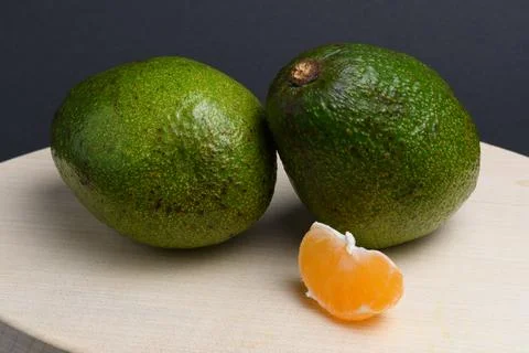 Two avocados and a slice of tangerine on a cutting board Stock Photos