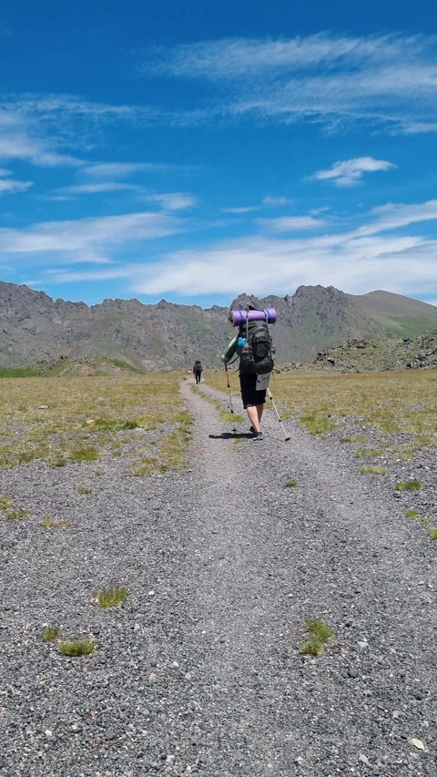 Two backpackers hiking on trail in high altitude mountain valley. Vertical video Stock Footage 282044555