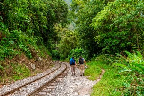 Two backpackers walk along the railroad tracks that enter the Urubamba jungle Stock Photos