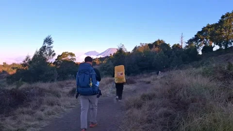 Two backpackers walking on a mountain trail at sunrise Stock Footage 342095592