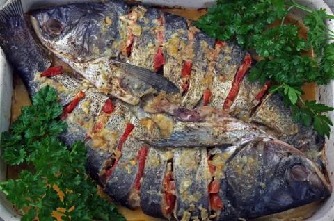Two baked fish stuffed with vegetables and decorated with parsley Stock Photos