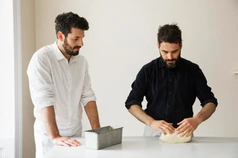 Two bakers standing at a table, kneading bread dough, a metal baking tin. Stock Photos