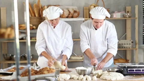 Two bakers work together to prepare raw dough and weigh it on scales to make Stockbeeldmateriaal 306704961