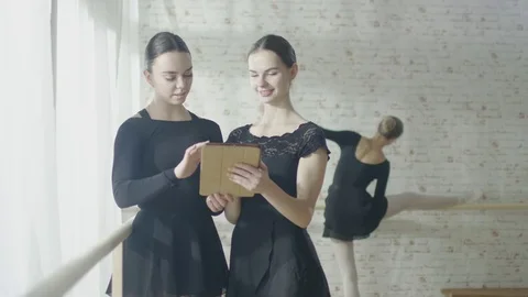 Two Ballerinas Using Tablet Computer While Third Exercises on the Barre Stock Footage 71625128