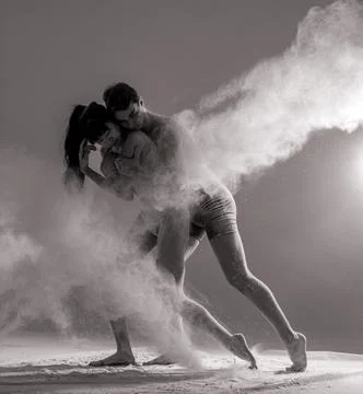 Two ballet dancers perform dance against background of white flour cloud in a Stock Photos