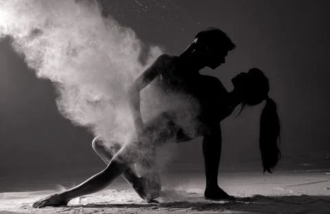 Two ballet dancers perform dance against background of white flour cloud in a Photos