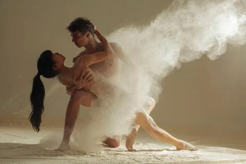 Two ballet dancers perform dance against background of white flour cloud in a Photos